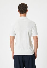 Biała krótko rękawowa koszulka polo, żebrowana faktura, z kołnierzykiem i prostym dołem. Prosty design, odpowiednia do casualowego noszenia.