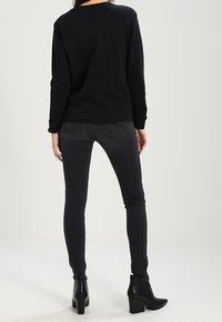 Sudadera negra con escote redondeado, combinada con vaqueros ajustados de color gris oscuro. Botines negros de tacón con un acabado texturizado.