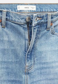 Light blue denim jeans feature a zip fly, bronze button closure, and copper rivets. The fabric has a slightly textured surface.