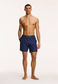 Tmavě modré plavky s potiskem palem, elastickým pasem a nastavitelným šňůrkovým stahováním, vyrobené z lehkého, rychleschnoucího materiálu.