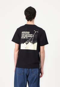 Black cotton T-shirt featuring a vintage-style lawnmower graphic in cream on the back, with text and a distressed finish.