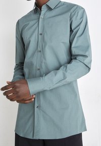 Camicia teal con bottoni, realizzata in tessuto liscio, con colletto aperto, maniche lunghe e polsini con bottoni, con orlo curvo.