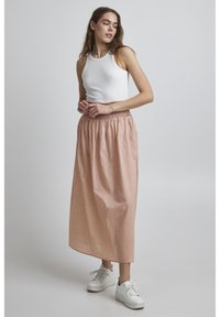 Gonna maxi di un delicato rosa chiaro con un motivo sottile, vita elasticizzata e design fluido, abbinata a una canotta bianca e sneakers bianche.