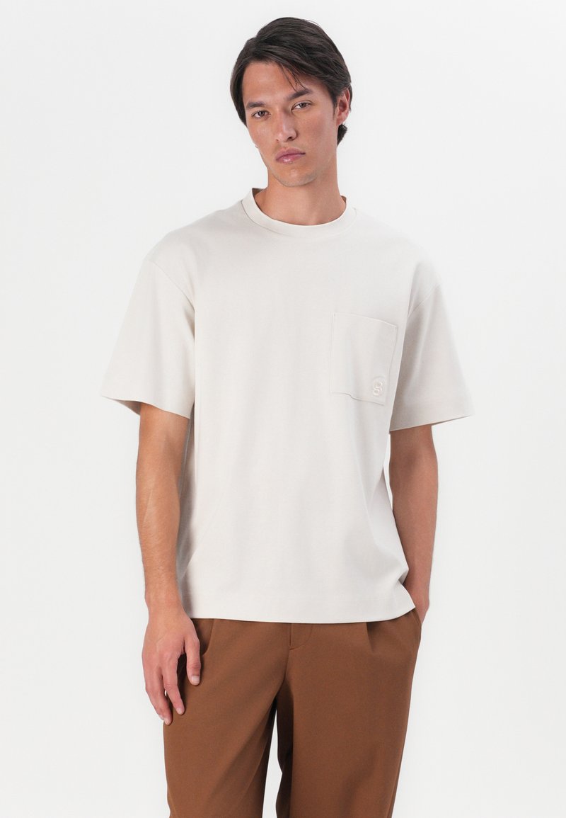 Beżowa bawełniana koszulka z okrągłym dekoltem, krótkimi rękawami i kieszonką na piersi z dyskretnym haftem logo.