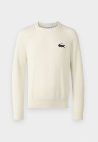 Cremfarbener Rippstrickpullover mit langen Ärmeln, Rundhalsausschnitt und Lacoste-Logo auf der Brust. Hergestellt aus strukturiertem Stoff.