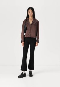 Brown satin button-up shirt with long sleeves, paired with black flare jeans and chunky black shoes. Small black bag worn across the shoulder.