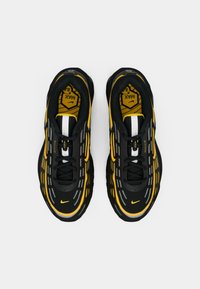 Zwarte en gele sportieve schoenen met een gestructureerde bovenkant, voorzien van een verhoogde zool, reflecterende accenten en een opvallend vetersysteem.