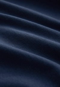 Țesătură de un albastru închis, cu o textură moale și netedă, care prezintă pliuri și valuri delicate. Materialul pare ușor lucios și ușor.