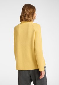 Gelber gerippter Strickpullover mit hohem Kragen und langen Ärmeln, der einen lockeren Schnitt und strukturierten Stoff aufweist.