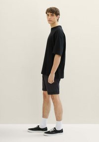 Czarna, luźna koszulka z krótkim rękawem, połączona z ciemnymi szortami. Na stopach czarne trampki z białymi akcentami. Widać białe skarpetki.