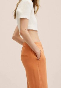 Hvid cropped sweater med korte ærmer og orange skræddersyede bukser med sidelommer og en glat tekstur.