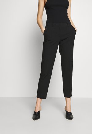 Schwarze, taillierte Hose mit slim Fit, seitlichen Taschen, glatter Textur und verkürzter Länge. Kombiniert mit schwarzen Mules.