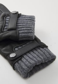 Black leather gloves with gray ribbed knit cuffs and adjustable leather straps with metal snap buttons.