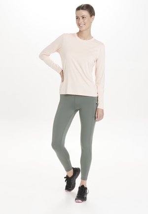 Lyserød langærmet top kombineret med olivengrønne leggings. Leggingsene har sidelommer og er lavet af strækbart, tætsiddende materiale.
