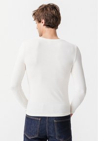 Camicia bianca a maniche lunghe realizzata in materiale leggero, con scollo rotondo e design aderente, abbinata a jeans blu scuro.