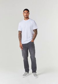 Bela bombažna majica in sive kavbojke, s sivimi supergami. Majica ima okrogel izrez, kratke rokave in ohlapen kroj.