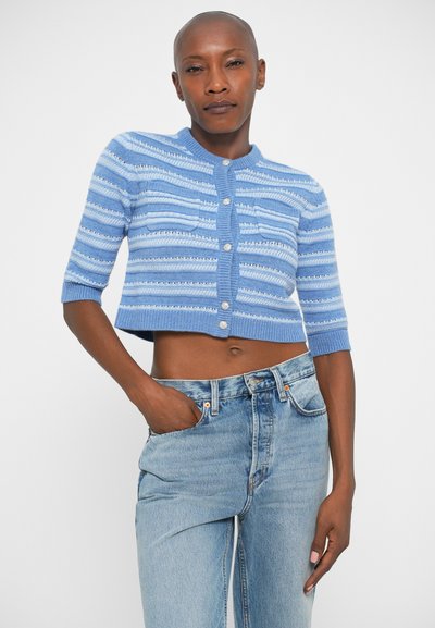 Gilet court bleu clair avec des rayures horizontales et des accents texturés. Doté d'une fermeture à boutons et de manches courtes. Associé à un denim léger.