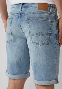 Shorts en denim bleu clair avec des ourlets roulés, présentant deux poches arrière, une patch en cuir marron et des détails légèrement usés.