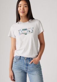 Grå kortärmad T-shirt med en blommig Levi's-logotypgrafik, tillsammans med ljusblå denimjeans med en klassisk femficksdesign.