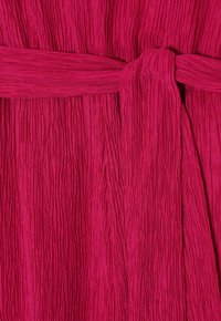 Tessuto fucsia testurizzato con pieghe verticali, caratterizzato da un dettaglio con cintura annodata per un effetto arricciato. Materiale liscio e leggero.