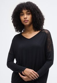 Μαύρο μακρυμάνικο μπλουζάκι με V λαιμόκοψη από απαλό ύφασμα, με δαντέλα στους ώμους, λεία υφή και άνετη εφαρμογή.