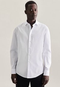 White long-sleeve shirt with a button-down collar, featuring a smooth texture and curved hem. It has a fitted design and visible buttons.