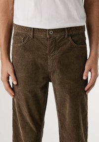 Pantalones de pana marrón con corte recto, que presentan un cierre de botón, cinco bolsillos y un patrón acanalado texturizado.