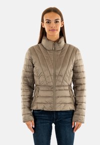 Veste rembourrée de couleur beige clair avec un col haut, fermeture éclair et coutures verticales, dotée de deux poches latérales avec des zips.