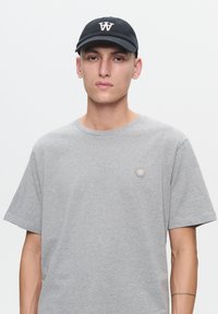 T-shirt in cotone grigio con scollatura rotonda e maniche corte, con un piccolo logo beige sul petto. Cappellino da baseball nero con logo bianco.