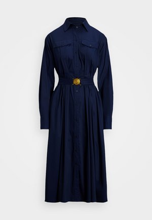 Robe chemise bleu marine en tissu avec des fermetures à boutons, deux poches poitrine, une taille ceinturée avec une boucle dorée et des manches longues.