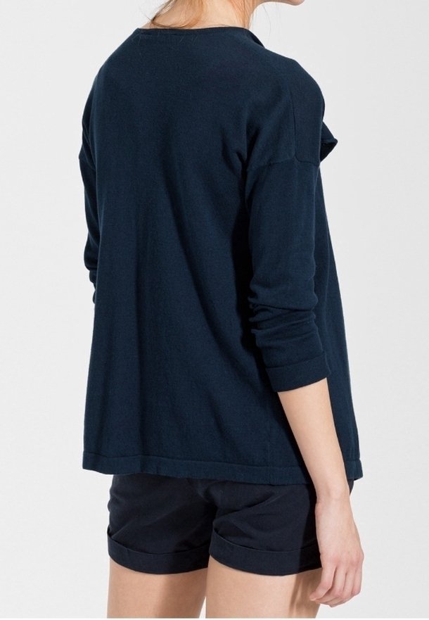 Femme portant un haut ample à manches longues bleu marine foncé avec des manches retroussées et un short assorti bleu marine foncé à ourlet roulé, de dos.