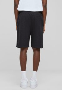 Pantalones cortos deportivos negros confeccionados en una tela suave, con un ajuste relajado, cinturilla elástica y dos bolsillos laterales. Combinados con zapatillas blancas.
