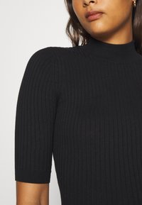 Black ribbed knit top with a high neck and short sleeves, featuring a textured pattern throughout the fabric.