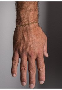 Gold chain bracelet on a wrist of a hand with visible hair and skin texture. The hand is oriented palm down, showing fingers clearly.