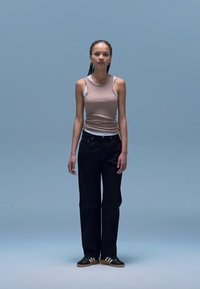 Camisola de alças bege, jeans pretos de cintura alta e ténis pretos com riscas brancas. Fundo simples com iluminação suave.