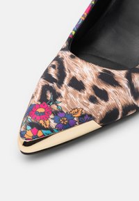 Chaussure plate à bout pointu avec imprimé léopard, accents floraux colorés et bordure métallique dorée sur la pointe.