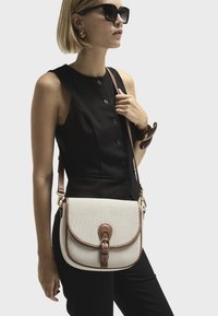 Beige canvas crossbody bag with brown leather accents, featuring a buckle closure and adjustable strap. Smooth texture, rectangular shape.