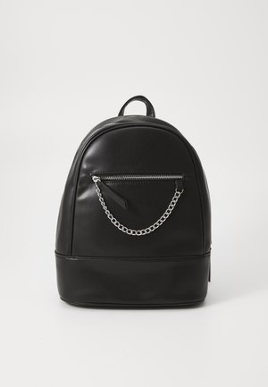 Sac à dos compact en cuir noir avec poche zippée à l'avant et chaîne argentée décorative sur un fond clair uni.