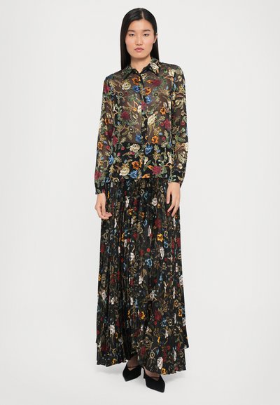 Zwarte doorzichtige bloemenblouse gelaagd over een geplooide zwarte rok, versierd met kleurrijke bloemenpatronen. Heeft een kraag en lange mouwen.