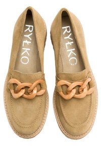 Beżowe zamszowe loafersy z błyszczącym, przerośniętym łańcuchem na przodzie. Okrągły nos, przeszycia i płaska podeszwa.
