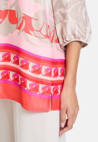 Bunte gemusterte Bluse in pink, rot und beige mit Schlagärmel und einem seitlichen Schlitz für mehr Bewegungsfreiheit.