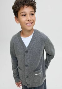 Pelēks kardigāns ar V-veida kaklu, ribots piedurknes, trim pogām un divām priekšējām kabatām ar izšuvumu. Mīksta tekstūra un viegla konstrukcija.