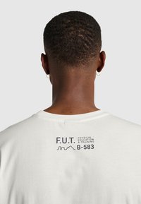 Hvid t-shirt med screenprint på ryggen med "F.U.T. FYSISK UDDANNELSE & TRÆNING B-583" i sort tekst. Korte ærmer, bomuldsstof.