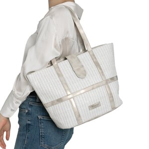 Mujer con blusa blanca y vaqueros azules lleva un gran bolso tote blanco tejido con detalles beige sobre el hombro.
