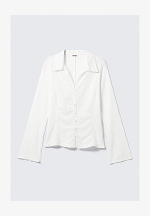 Λευκό πουκάμισο με μακριά μανίκια και γιακά, εφαρμοστή γραμμή, υφή υφάσματος, κούμπωμα με κουμπιά μπροστά και φουσκωτά μανίκια. Ορατή ετικέτα μάρκας.