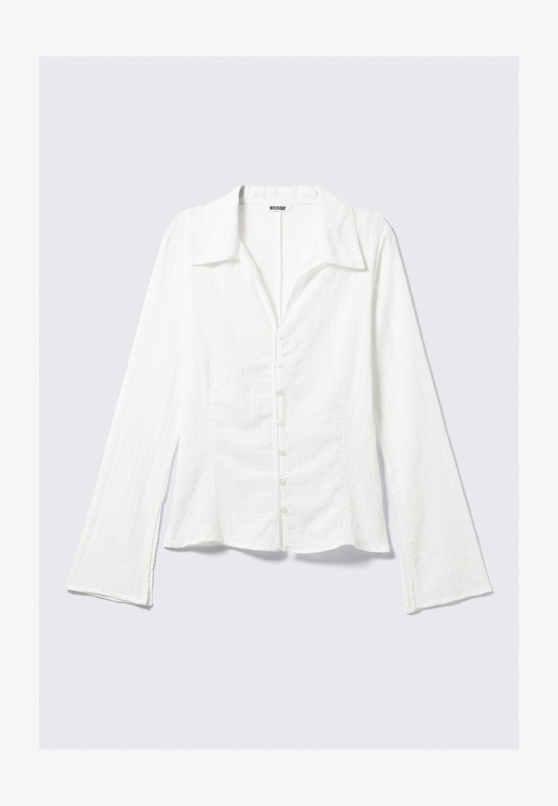 White long-sleeve shirt with a collar, fitted design, textured fabric, front button closure, and flared sleeves. Brand label visible.