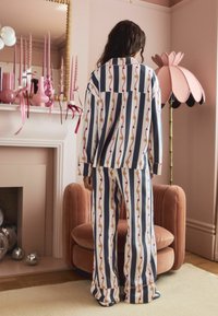 Lang pyjamasæt i vertikale striber i blå, hvid og rød med guldstjernes mønster. Blødt stof og løs, afslappet pasform.