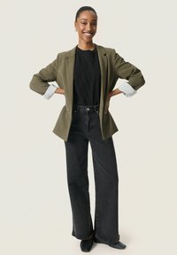 Blazer verde măsliniu peste o cămașă neagră, asociat cu blugi negri cu talie înaltă și pantofi negri. Închidere cu nasture la pantaloni, mâneci cu tiv.