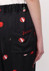 Svarte bukser i stoff med løs passform, elastisk liv og en sidelomme med rød brodert "fioruca." Dekorert med fargerike leppetrykk.