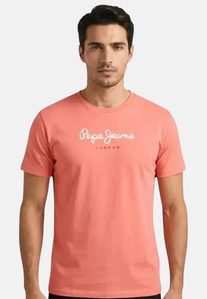Uomo che indossa una t-shirt a maniche corte color corallo Pepe Jeans London, rivolto in avanti su uno sfondo bianco semplice.